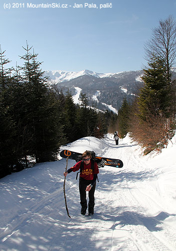 Jana si nese snowboard napříč a opírá se o čerstvě ulomenou větev