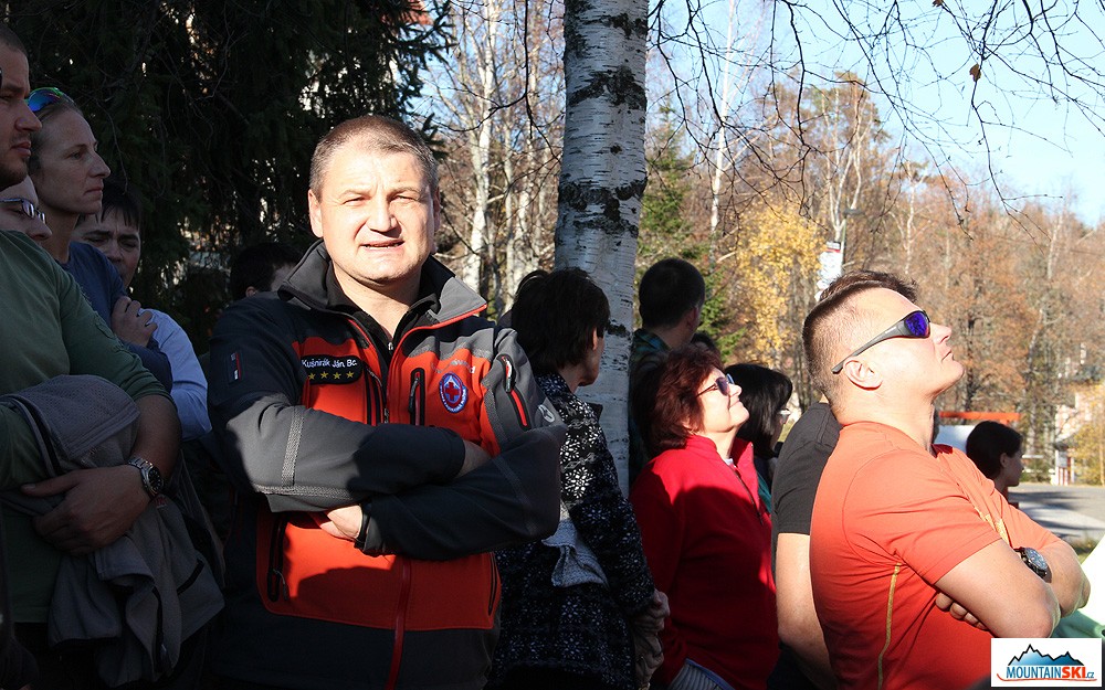 Všichni sledují pohyb záchranáře se psem ve vzduchu a náčelník vysvětluje, co se děje